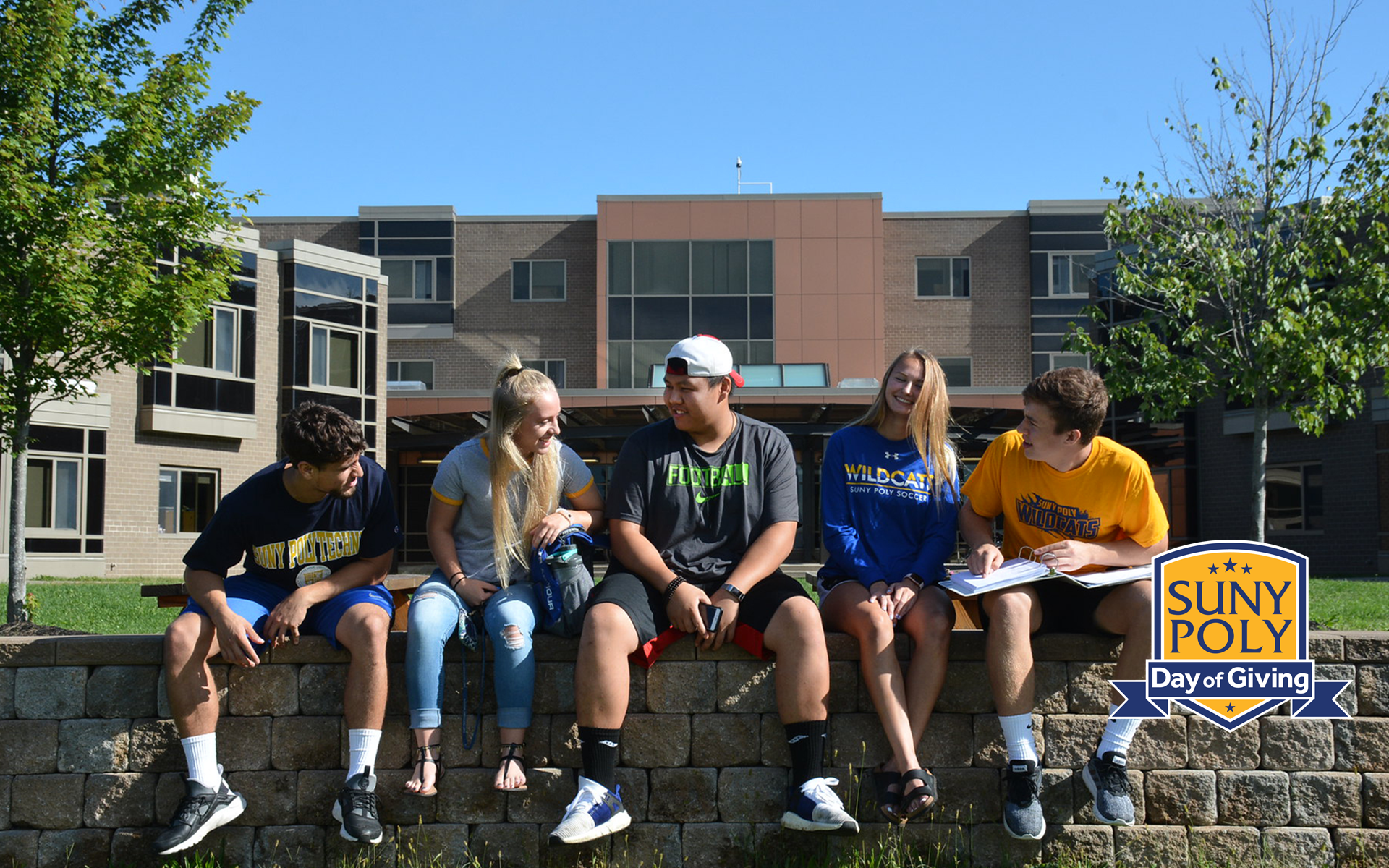 students sitting on a stone wall on campus